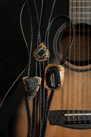 Bolo tie hanging on an acoustic guitar with a dark background