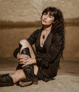 Woman in black outfit sitting on the ground against a textured wall.
