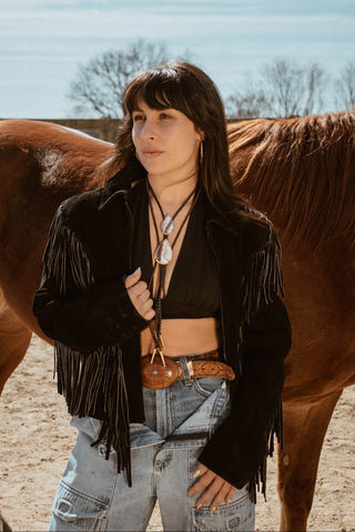 Woman in a black fringe jacket standing next to a horse outdoors